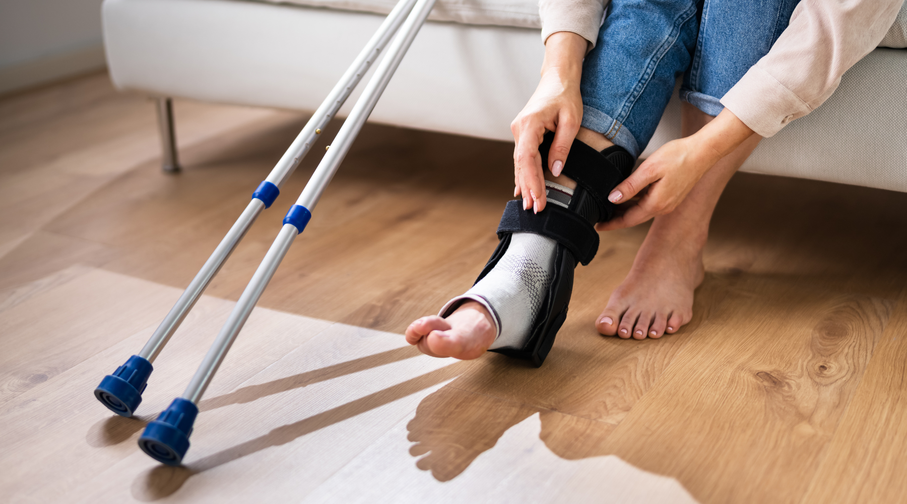 Woman with leg injury and crutches sitting on couch, preparing to use a space-saving tub-mount transfer bench for bathroom access