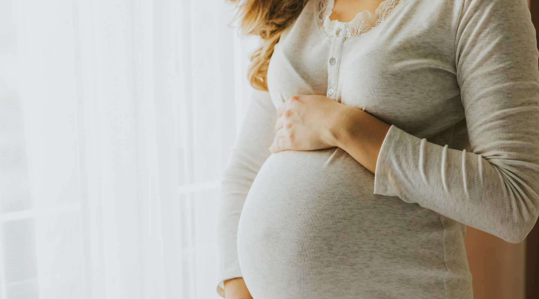 Pregnant woman holding belly while using a toilet-to-tub sliding transfer bench for safe bathtub access